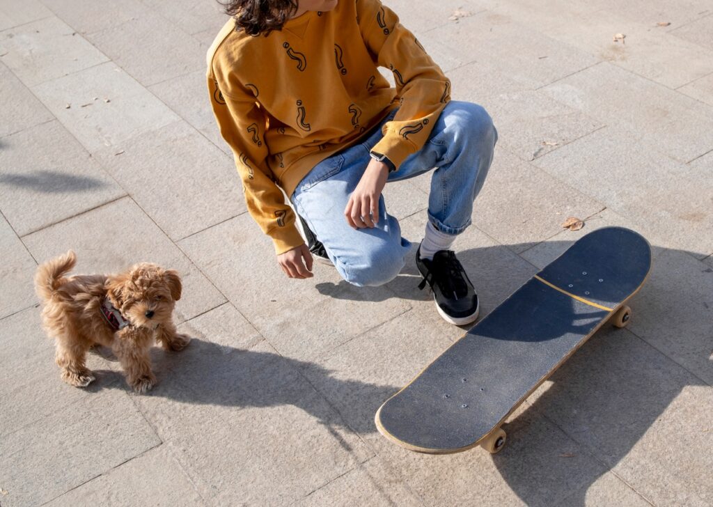 Kid squatting on a road with puppy and skateboard next to her